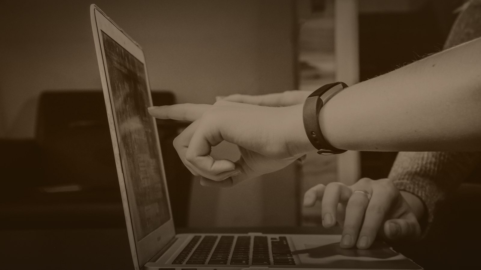 Sepia-toned photo of hands checking results on a laptop
